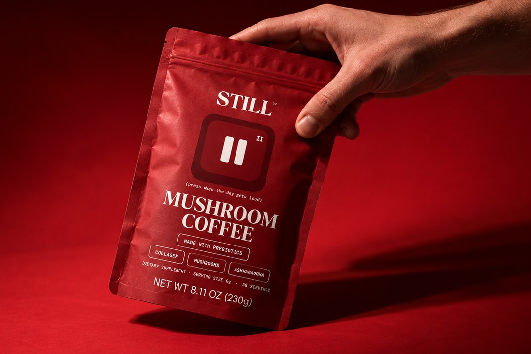 A hand holding a bag of STILL Mushroom Coffee against a red backdrop